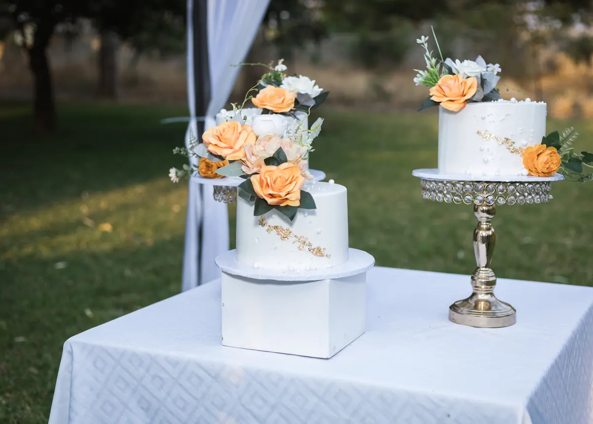 White wedding cakes decorated with peach flowers on an outdoor reception table